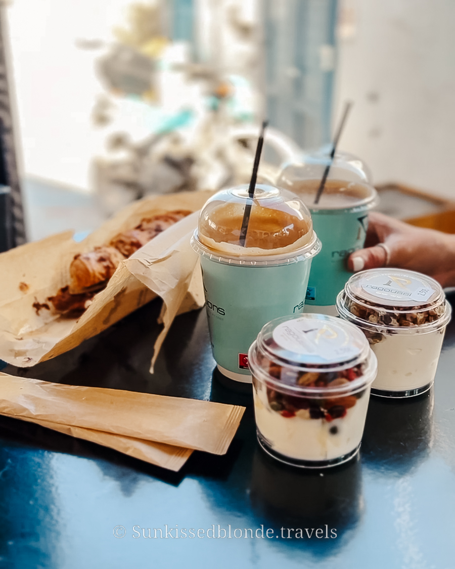 Breakfast spread at a Paros caf&eacute; featuring iced coffees, yogurt with granola, and a baked pastry on a black tabletop