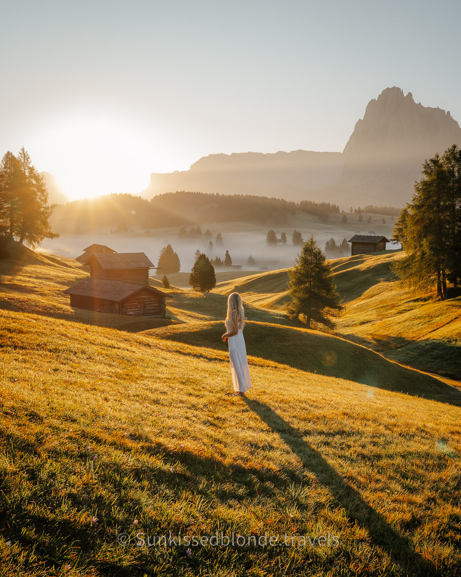 Woman Overlooking Golden hour light over Alpe di Siusi alpine meadow with Sassolungo mountain peaks in the background, Dolomites, South Tyrol, Italy