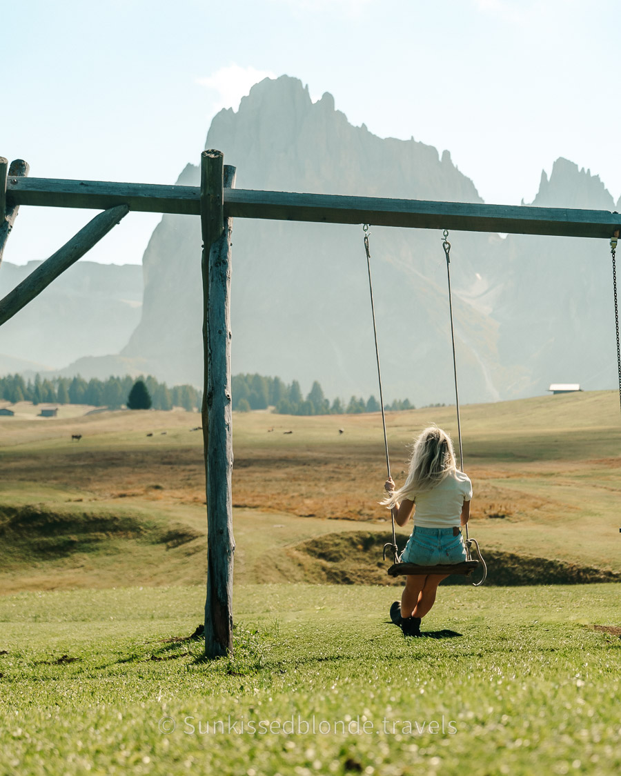Woman on Swing at Golden hour light over Alpe di Siusi alpine meadow with Sassolungo mountain peaks in the background, Dolomites, South Tyrol, Italy