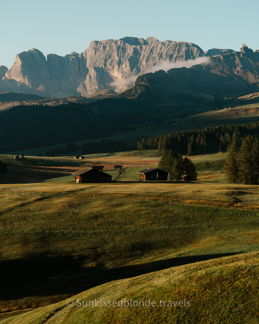 Huttes at Golden hour light over Alpe di Siusi alpine meadow with Sassolungo mountain peaks in the background, Dolomites, South Tyrol, Italy