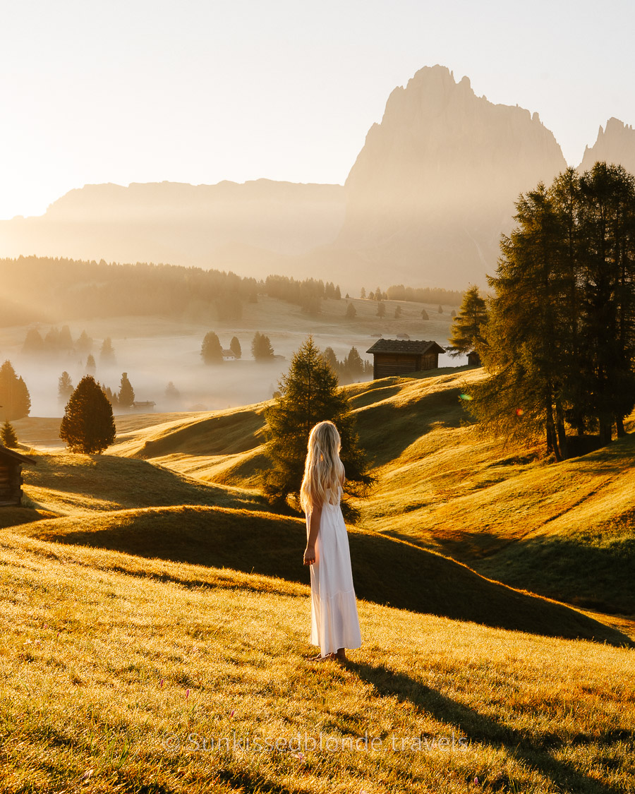 Woman looking over Golden hour light over Alpe di Siusi alpine meadow with Sassolungo mountain peaks in the background, Dolomites, South Tyrol, Italy